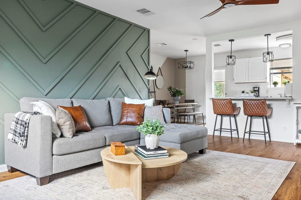 The chairs are adorned with patterned black-and-white throw pillows, and a small side table between them holds a wine bottle and some plants.