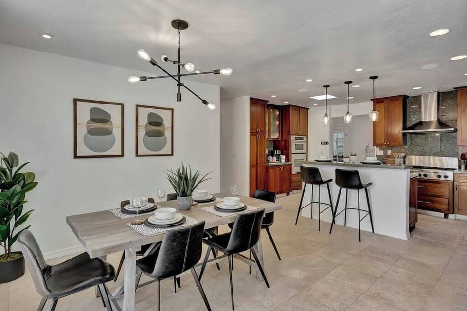 Modern dining area with seating for six adjacent to a kitchen featuring wood cabinetry and stainless steel appliances.