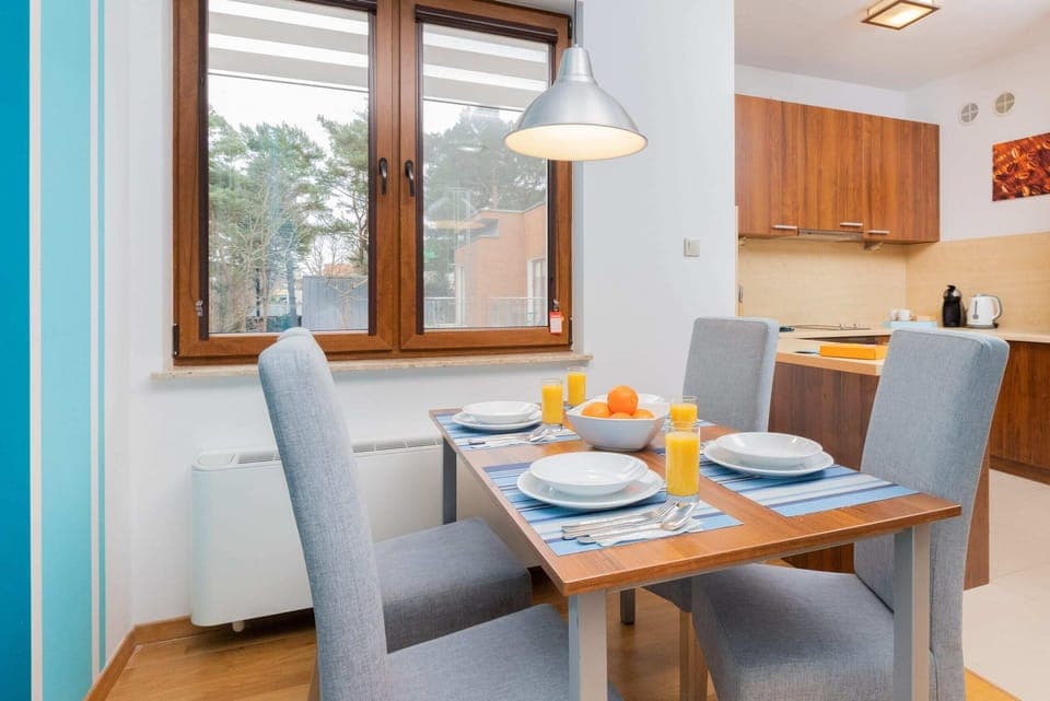  A dining area with a gray dining table and chairs. The room features large windows with bright blue curtains and a light-filled ambiance.