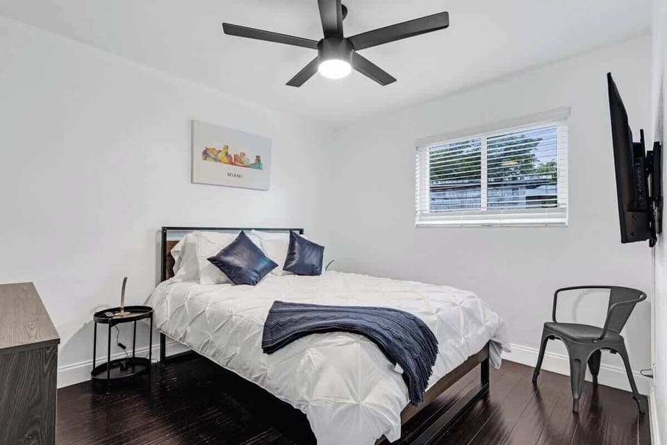 Cozy up in this clean, modern bedroom with blue accents, natural light, and a smart TV. Ideal for your Airbnb vacation—stylish, peaceful, and perfect for relaxing after a day of exploring.
