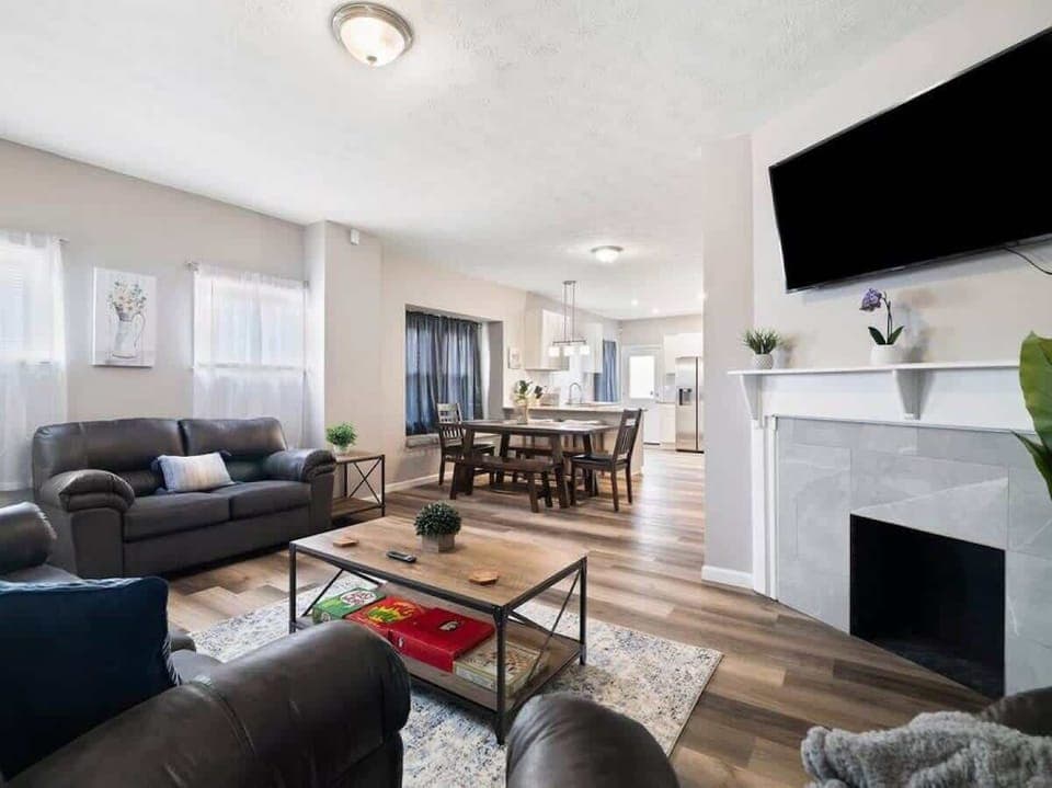 Step into this open-concept living area with cozy leather sofas, a stylish coffee table, and a modern fireplace topped by a wall-mounted TV. The space flows seamlessly into a dining area and bright kitchen for effortless entertaining! ️️