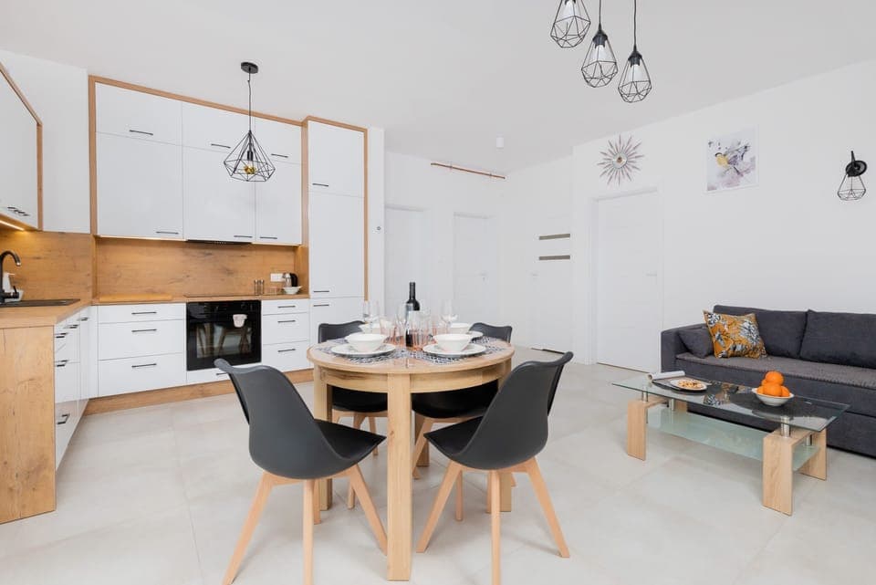 A dining area with a wooden table and four black chairs, surrounded by light decor and plenty of natural light.
