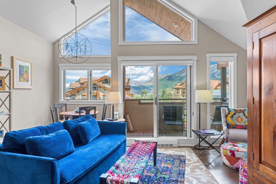 A vibrant blue velvet couch adds a pop of color to this cozy living room with a stunning mountain view.