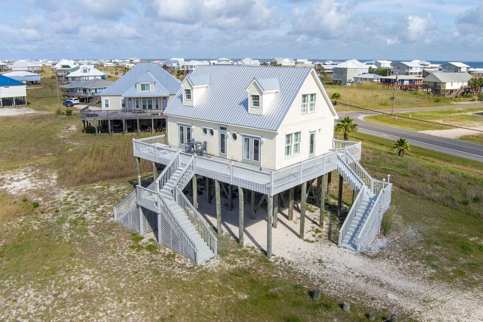 Elevated coastal home featuring wraparound decks and stairs, situated in a beachside community near the shore.
