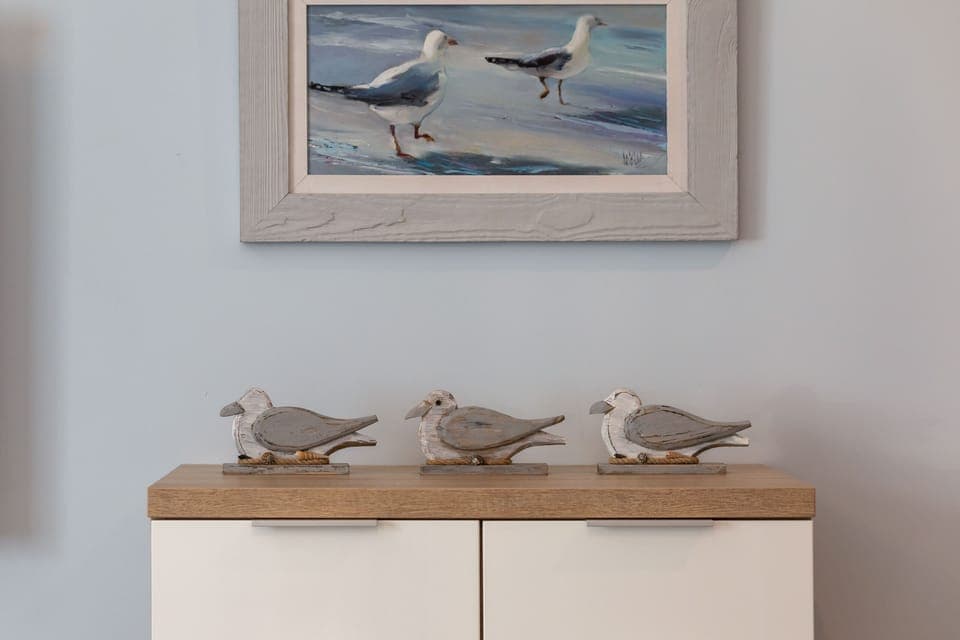 A wooden sideboard against a white wall, adorned with a framed picture, small plants, and a nautical-themed decoration.