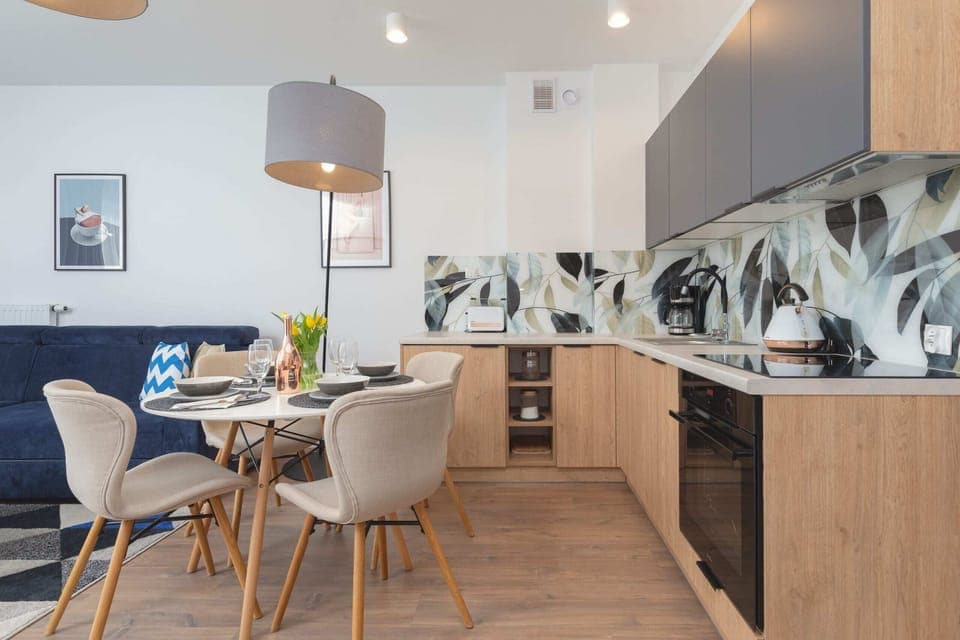 An open-plan kitchenette connected to a dining room with a table and colorful accents. The bright interior gives the impression of being fresh and modern.