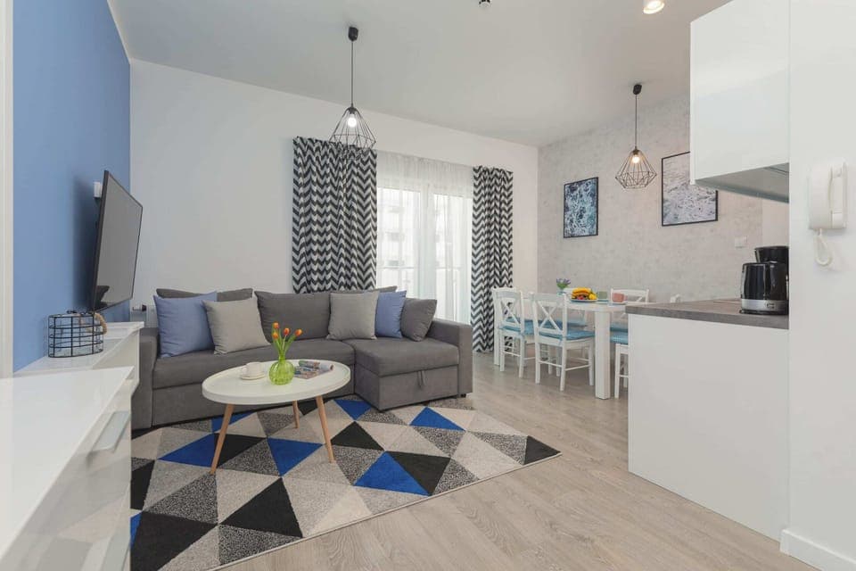 A cozy living room with a blue and gray theme, featuring a large sofa, a stylish rug, and a mounted TV. The decor gives a modern and welcoming feel.