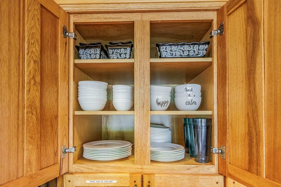 Spacious wooden kitchen cabinet with neatly organized dishware and bowls.