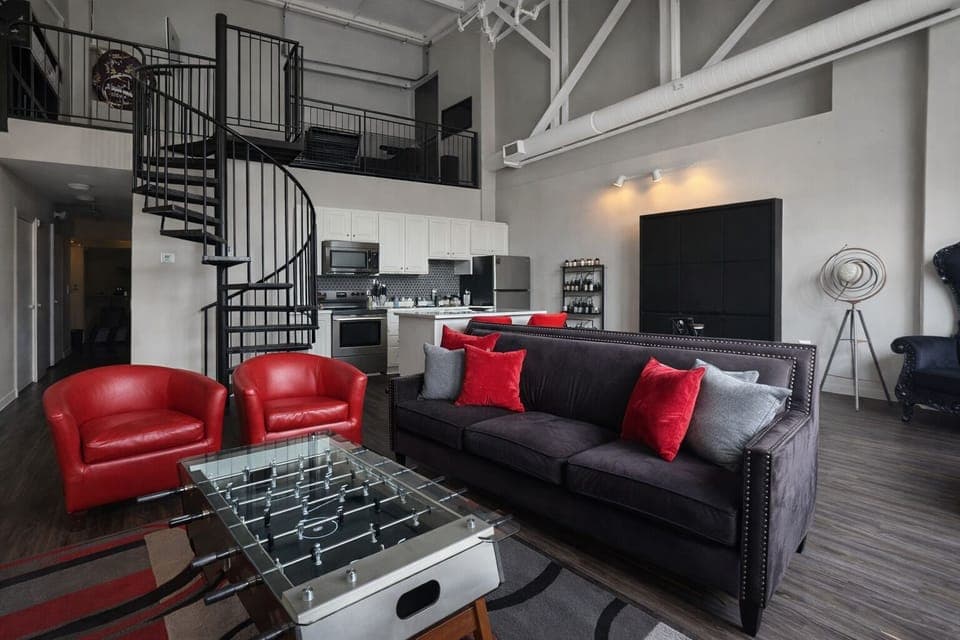 Bright and inviting living space with natural light pouring through large windows. Features comfortable seating, stylish décor, and a fun foosball table.