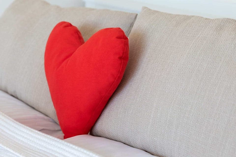 A cozy bed with white bedding and a decorative red heart-shaped pillow.
