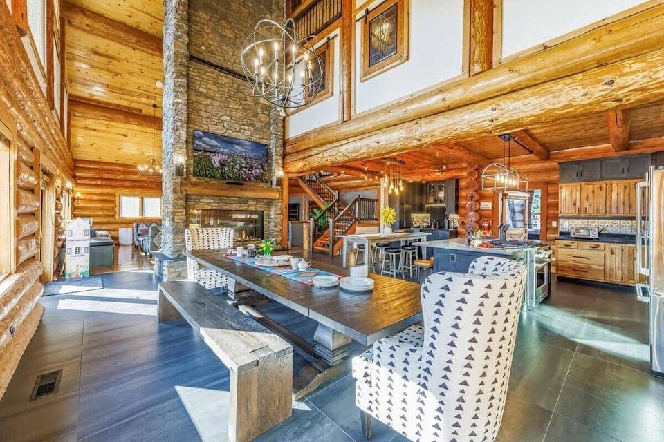 Spacious rustic log cabin interior featuring a huge gas two-way fireplace, vaulted wooden ceilings, and modern kitchen amenities.