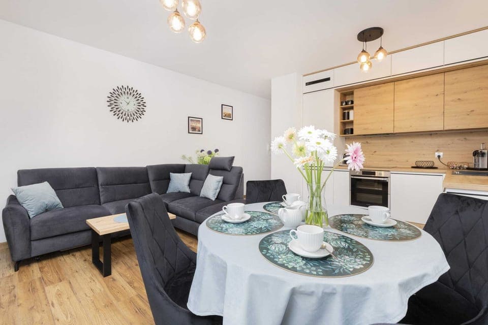 A spacious living room with a round dining table, elegant chairs, and a comfortable corner sofa.
