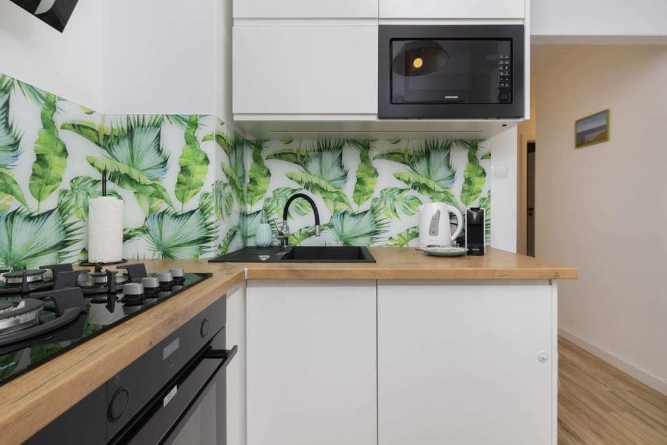 A well-equipped kitchen with a colorful backsplash featuring a tropical leaf design.
