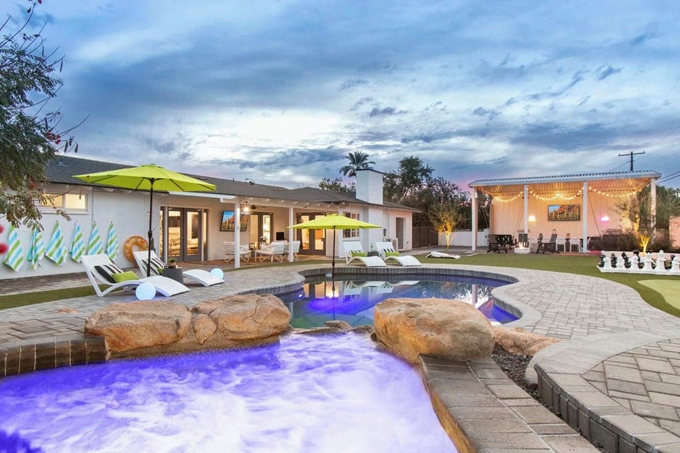Relax by the illuminated pool and hot tub in this spacious outdoor area with lounge chairs and a covered seating space.