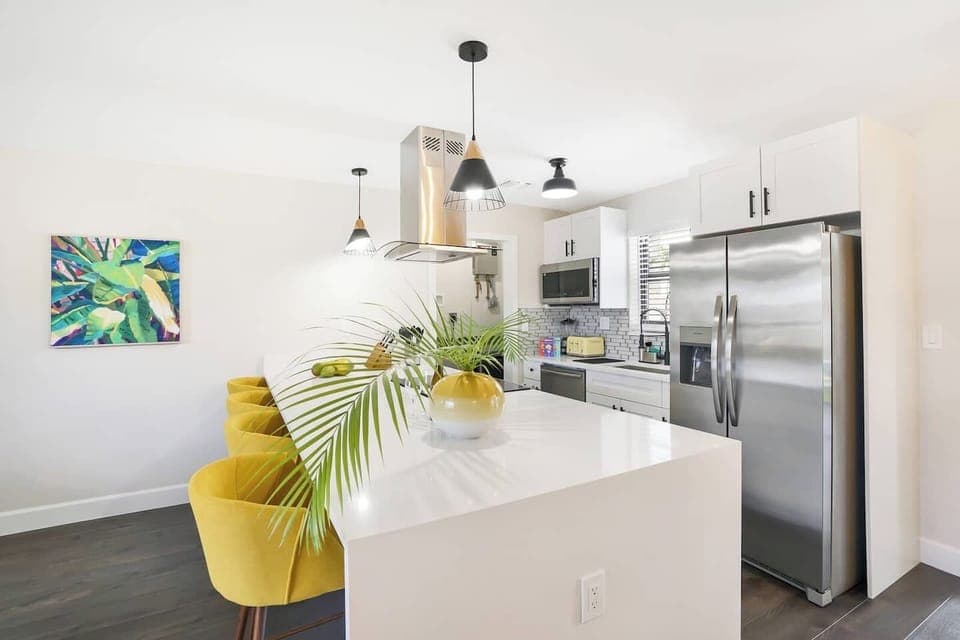Modern kitchen featuring stainless steel appliances, a spacious island with a waterfall edge, and sunny yellow barstools. The perfect space for cooking and entertaining