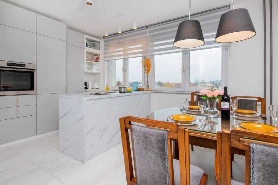 A spacious kitchen with white cabinets, a wooden dining table, and sleek gray chairs.
