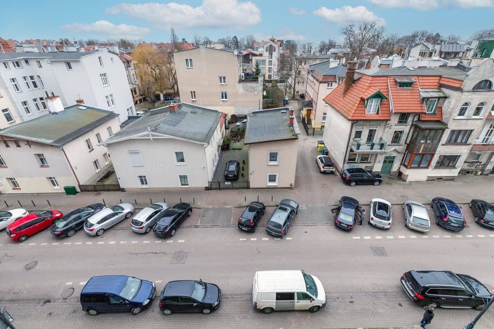 A view from above of a quiet residential area with parked cars and surrounding buildings.
