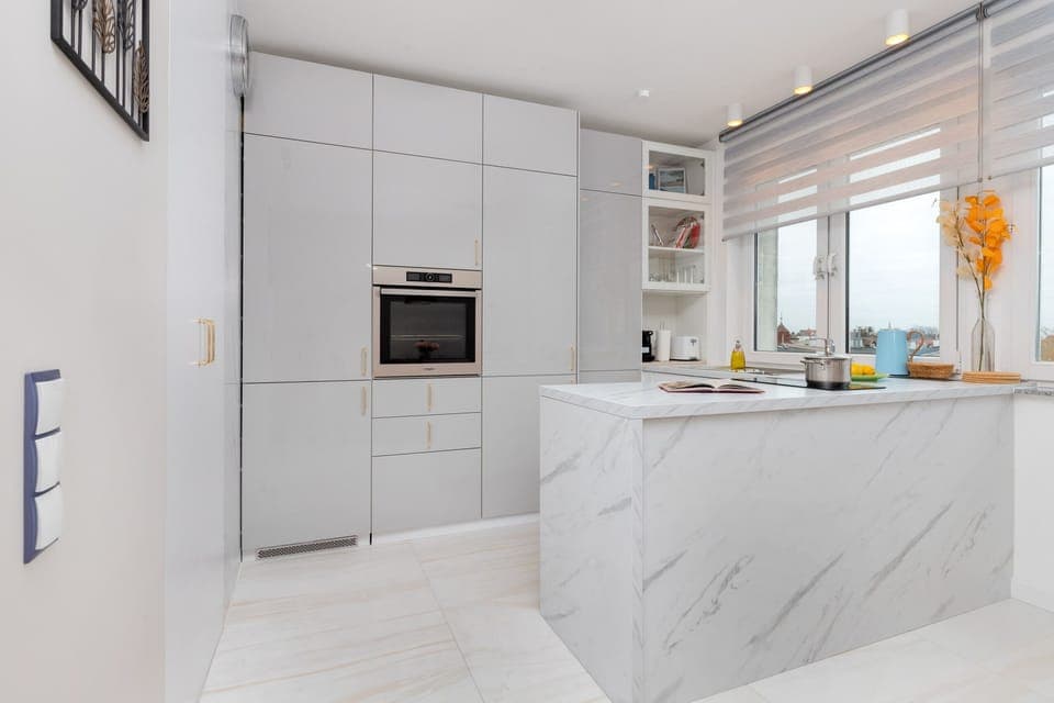 A sleek kitchen featuring a marble-topped island, white cabinetry, and modern appliances.
