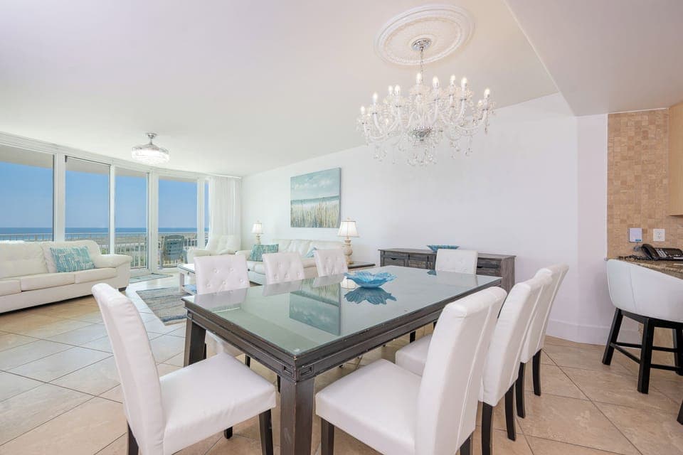 Bright and airy living space featuring a chic dining table, plush white sofas, and breathtaking coastal views