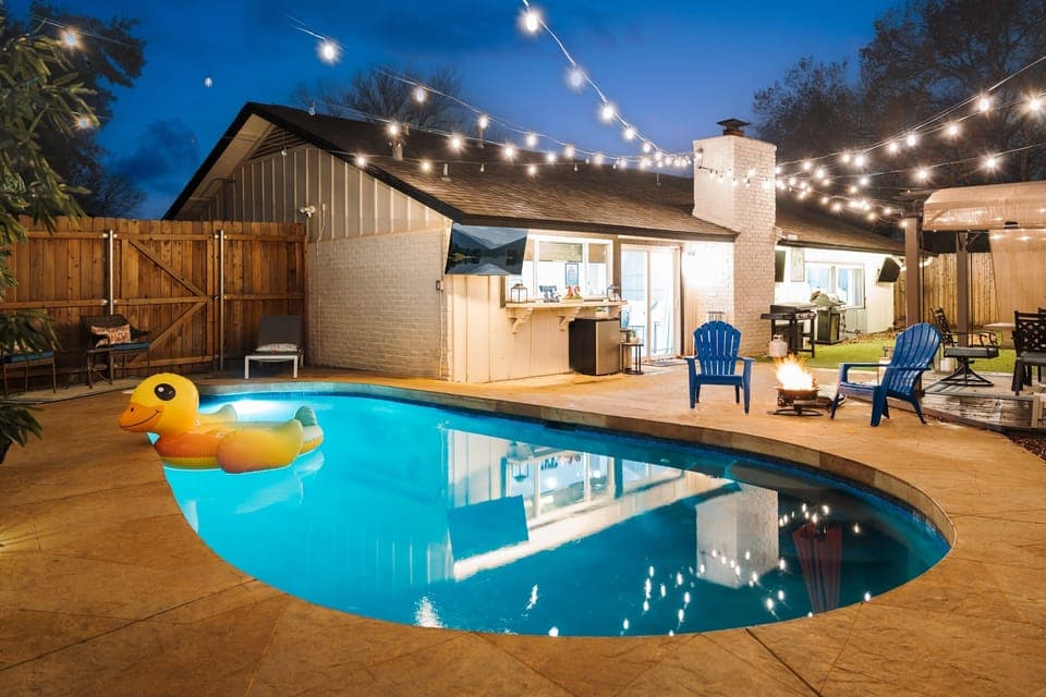 Unwind in a stunning backyard oasis featuring a sparkling pool with a fun duck floatie, cozy string lights, and ample seating. Perfect for evening swims and outdoor relaxation!