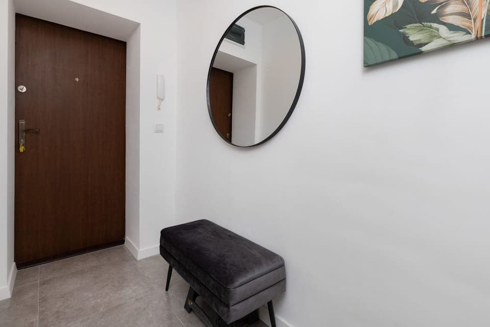 A hallway with a wooden front door, a round mirror, and a black bench for convenience.
