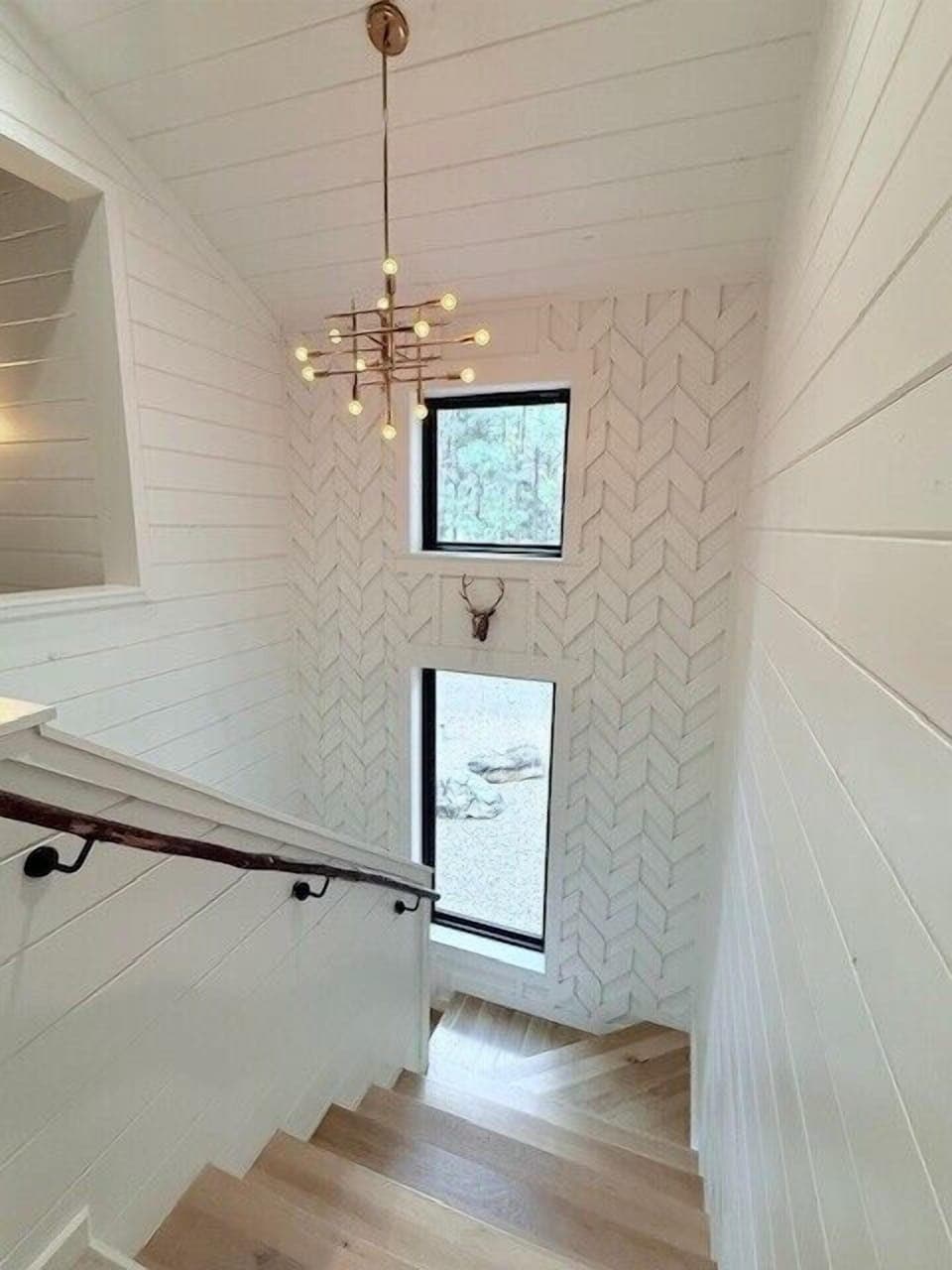 Ascend the stairs and be captivated by the seamless fusion of the stair accent wall, complementing the mid-century chandelier above with the breathtaking view of the forest outside.