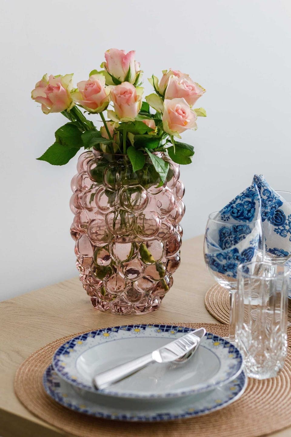 A close-up of a dining table set with decorative plates, glasses, and a vase with flowers.
