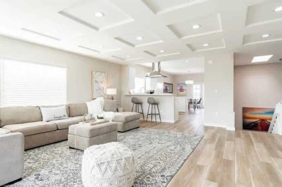 This living room features a cozy, sectional with soft neutral tones. The contemporary artwork on the wall adds a modern touch, complementing the room's elegant aesthetic. Natural light streams through large windows, enhancing the open and airy feel. 