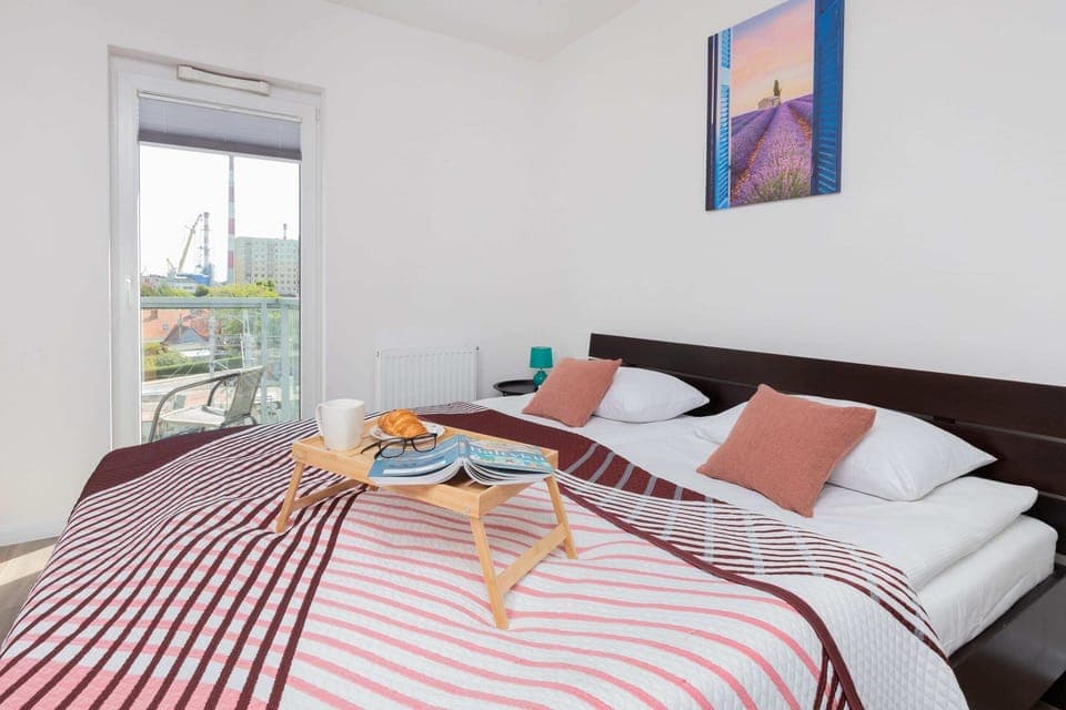 A sunny bedroom with a comfortable double bed, vibrant red-striped bedding, and modern decor.