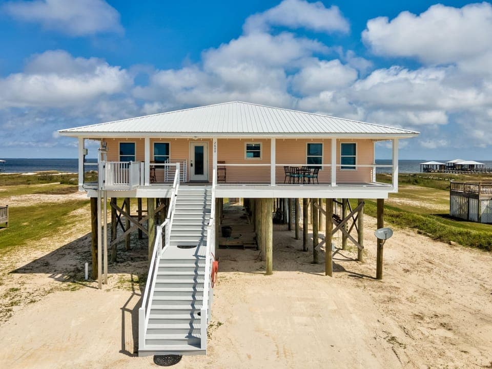 Coastal retreat on stilts with wraparound porch and beach access nearby.