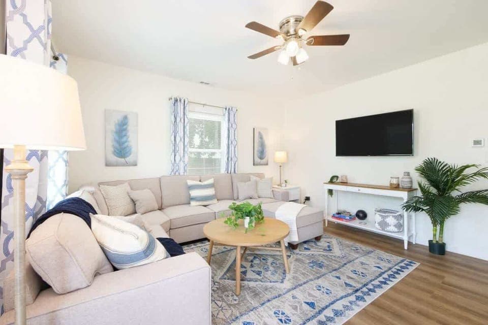 Bright living room w/ cozy seating, wall-mounted TV & natural light streaming through large windows