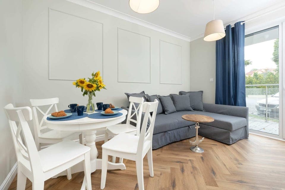 A bright dining and living area with a stylish gray sofa, blue accents, and a white dining set.

