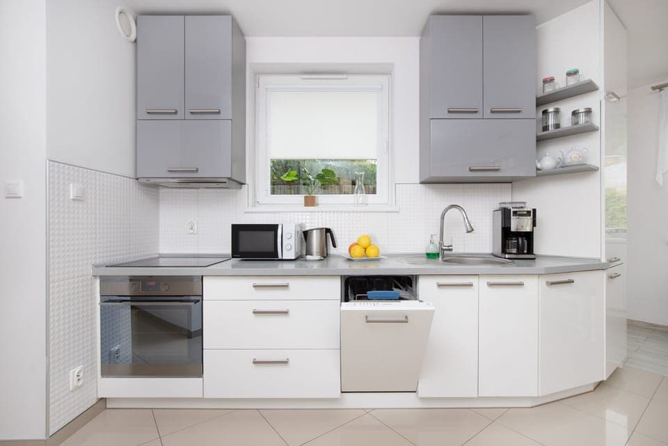 A modern kitchen with gray and white cabinets, a tiled backsplash, and essential appliances.