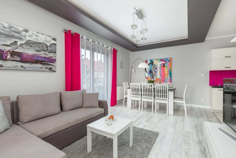 A modern and spacious living area with a comfortable gray sofa, bright pink accents, and a stylish coffee table, creating a vibrant and welcoming atmosphere.
