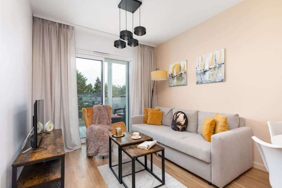 A bright living area with a cozy grey sofa, yellow accents, and a coffee table, perfect for relaxation.
