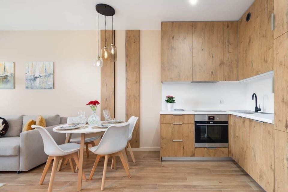A dining area with a round table, modern white chairs, and wooden kitchen cabinets creating a cozy atmosphere.
