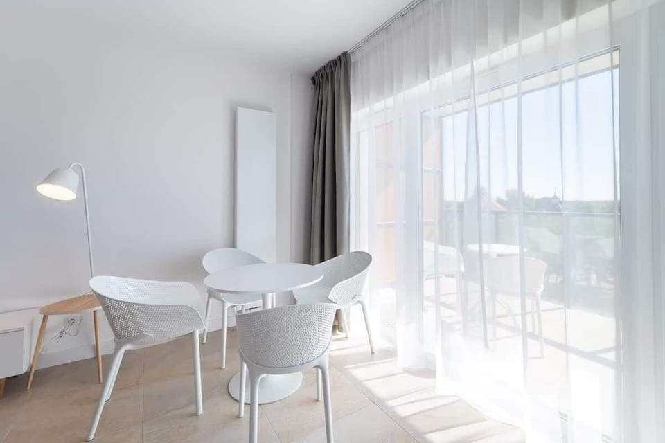 A dining area with a small white table and chairs, positioned near large windows for plenty of natural light.


