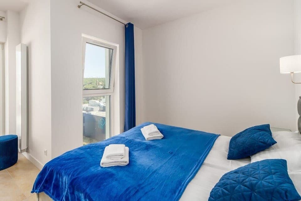 Another angle of the bedroom, showcasing large windows with curtains, allowing natural light to fill the space.
