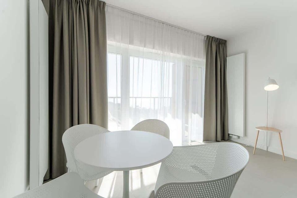 A minimalist dining area with a round table and modern white chairs, situated by large windows for plenty of natural light.
