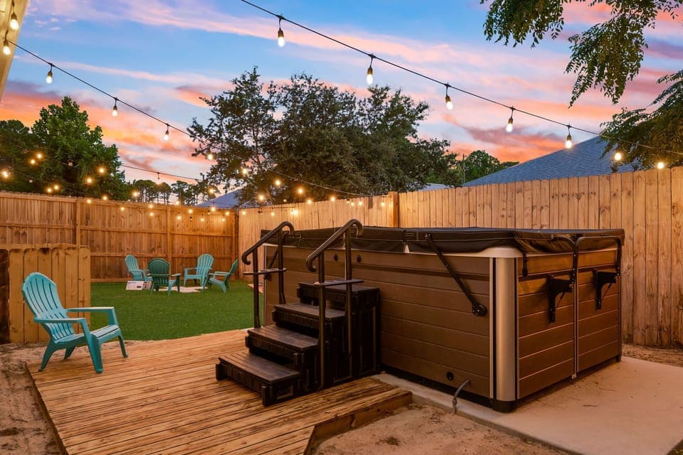 A cozy backyard oasis with a glowing hot tub, string lights, & relaxed seating.