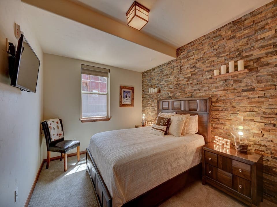 A modern decor queen size bedroom with a stone accent wall, with a window to shower the room with natural light