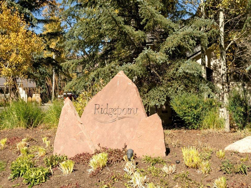 A stone sign with the engraved word "Ridgepoint" stands in a landscaped area with small plants and trees in the background.