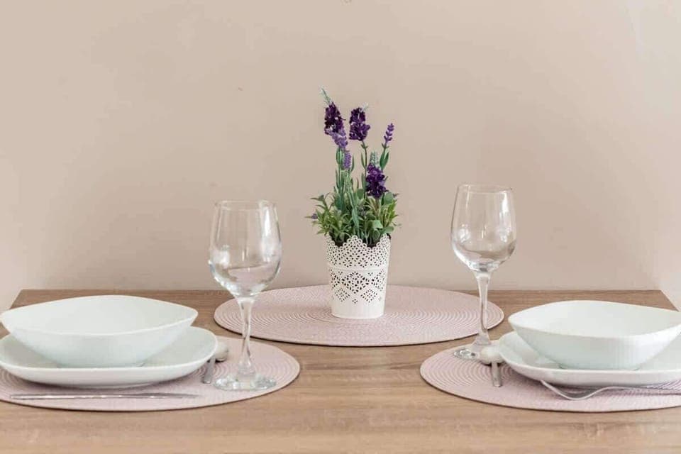 A close-up of a dining table set for two with white plates, glasses, and a floral centerpiece.

