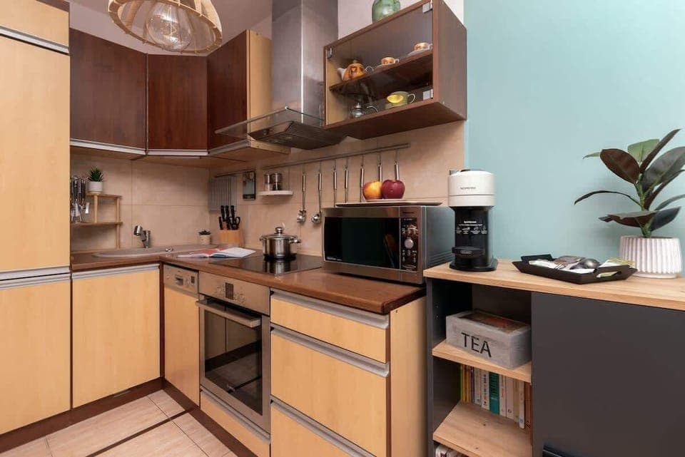A compact kitchen with wooden cabinets, tiled backsplash, and stainless-steel appliances, seamlessly integrated into the open-plan layout.

