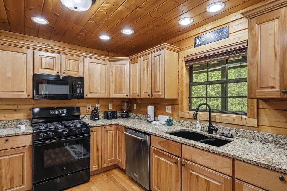 Your fully equipped kitchen features granite counters, gas stove, and dishwasher - perfect for preparing meals while enjoying forest views.