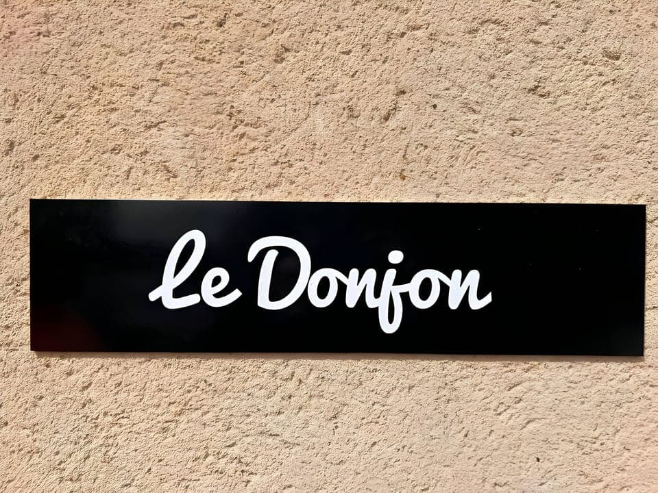 "Discover the elegant wall plaque in the "Le Donjon" apartment. A black plaque with the white inscription "Le Donjon" adding a touch of elegance and authenticity to the apartment's entrance."