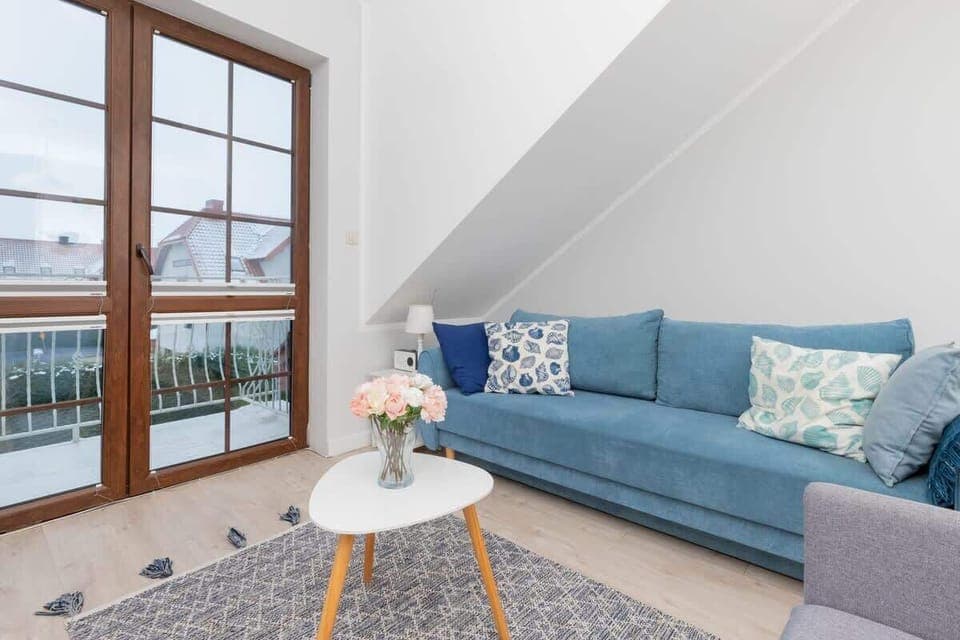 A cozy living area with blue sofas, nautical-themed pillows, and a coffee table, complemented by natural light from large windows.
