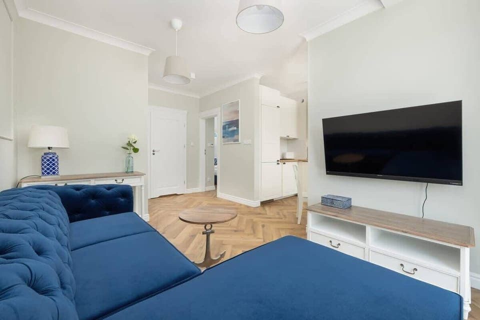 A modern living room with a navy blue sofa, a wall-mounted TV, and a chic coffee table.

