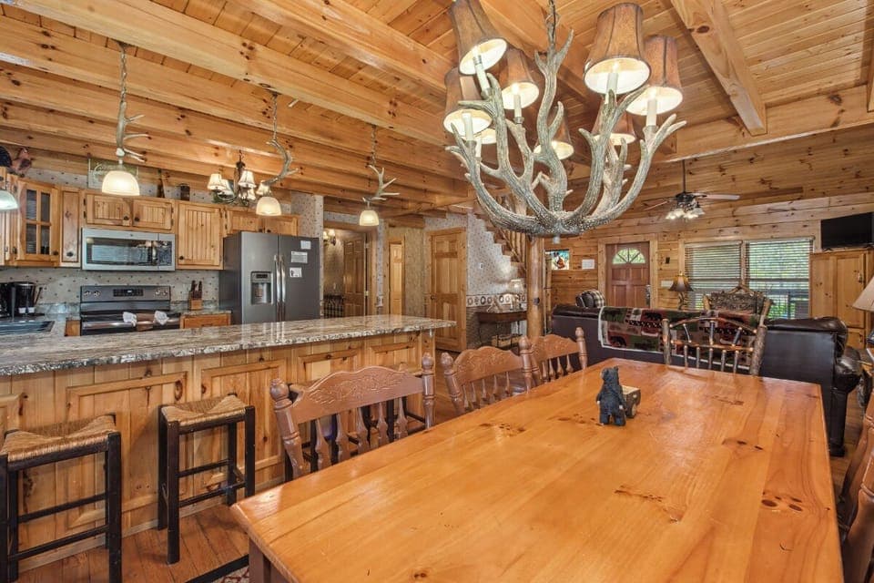 Rustic charm meets modern convenience in this stunning cabin kitchen and dining area, where you'll create memories around the handcrafted table beneath the antler chandelier.