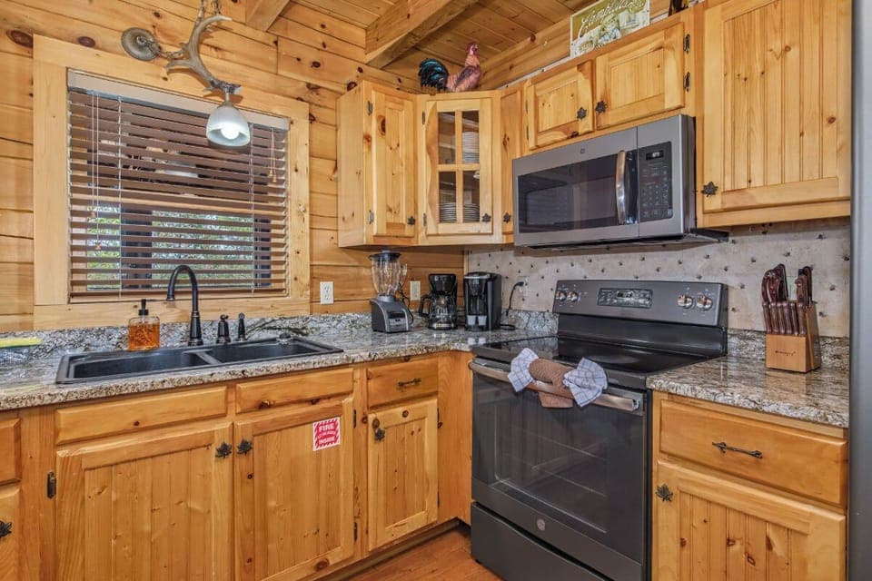 Your cozy cabin kitchen blends rustic charm with modern convenience—granite countertops and stainless appliances surrounded by warm pine.